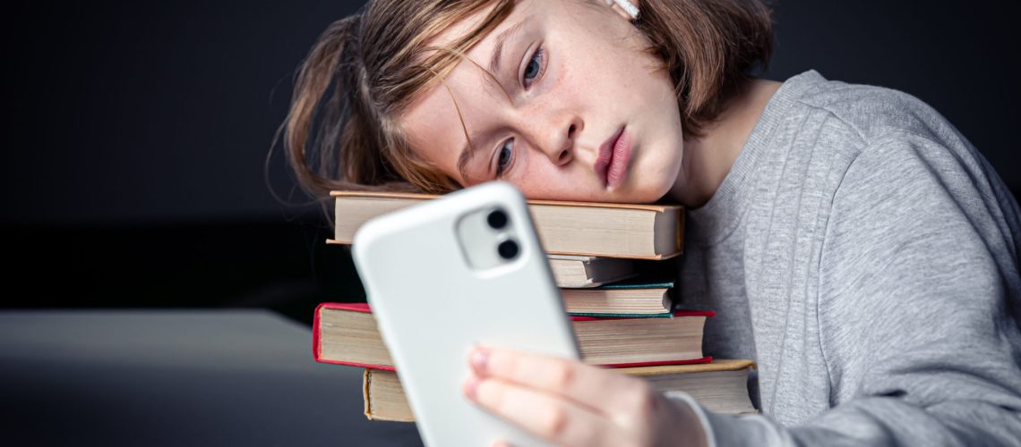 A little girl sits near books and takes a selfie, bored from reading.