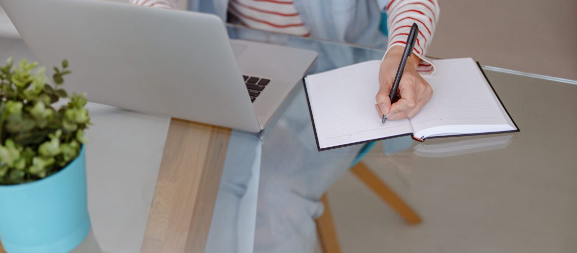 Woman using laptop and taking notes at home
