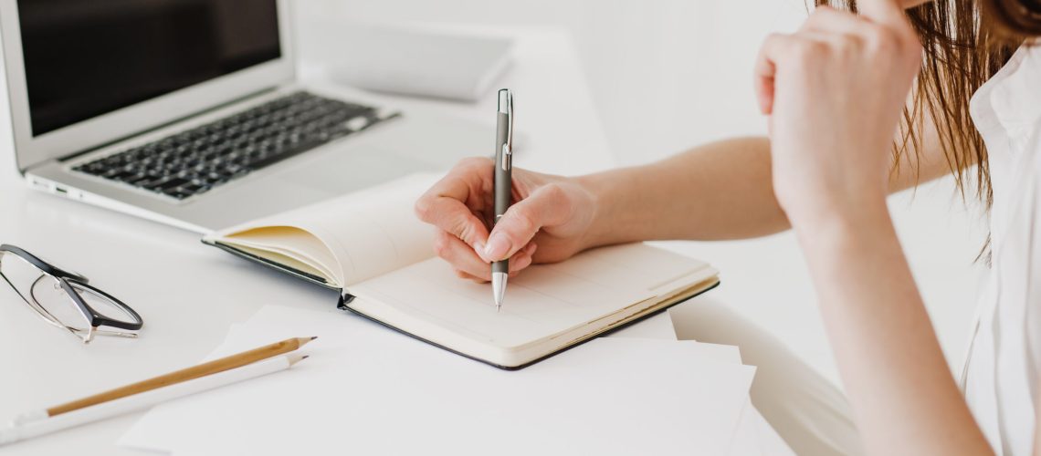 Unrecognizable woman making notes with a pen in a business notebook.